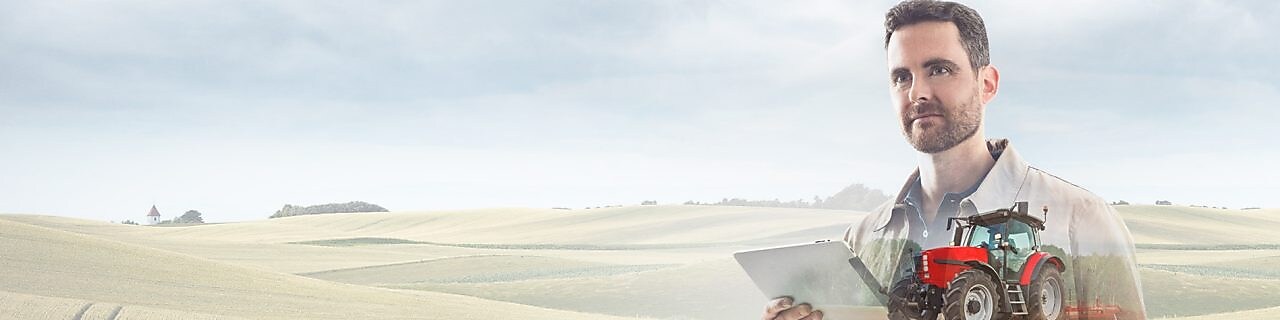 homme lisant un document dans un champ avec un tracteur rouge