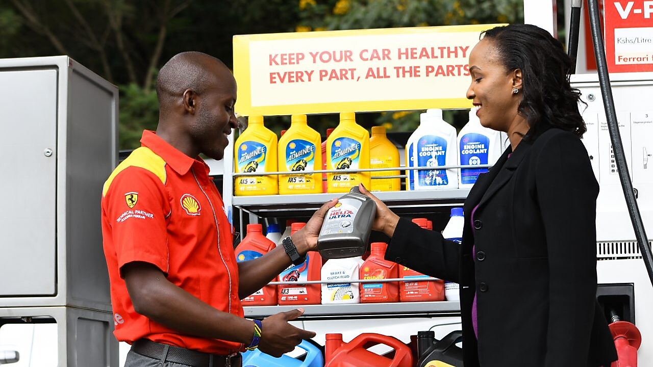A red Ferrari sitting on a Shell station forecourt with a man leaning on a petrol pump