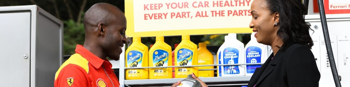 A red Ferrari sitting on a Shell station forecourt with a man leaning on a petrol pump